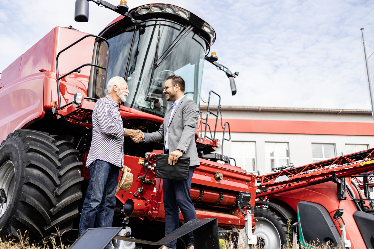 Farmer and dealer shaking hands after successful tractor purchase. Investing in farming equipment.